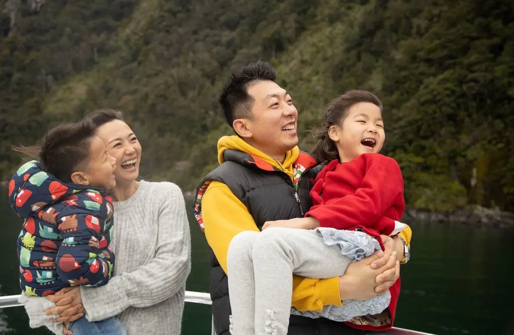A family on a cruise in Milford Sound, smiling and dressed warmly for the winter weather