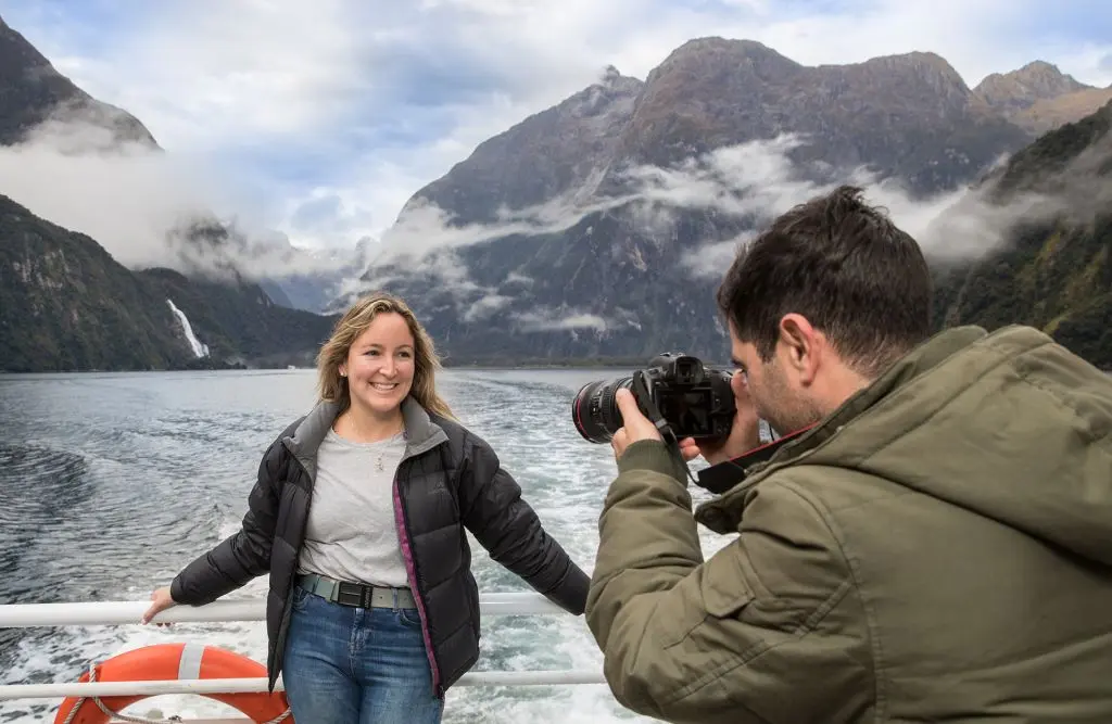 A couple on an autumn cruise in Milford Sound, with one person taking a photo of the scenery.